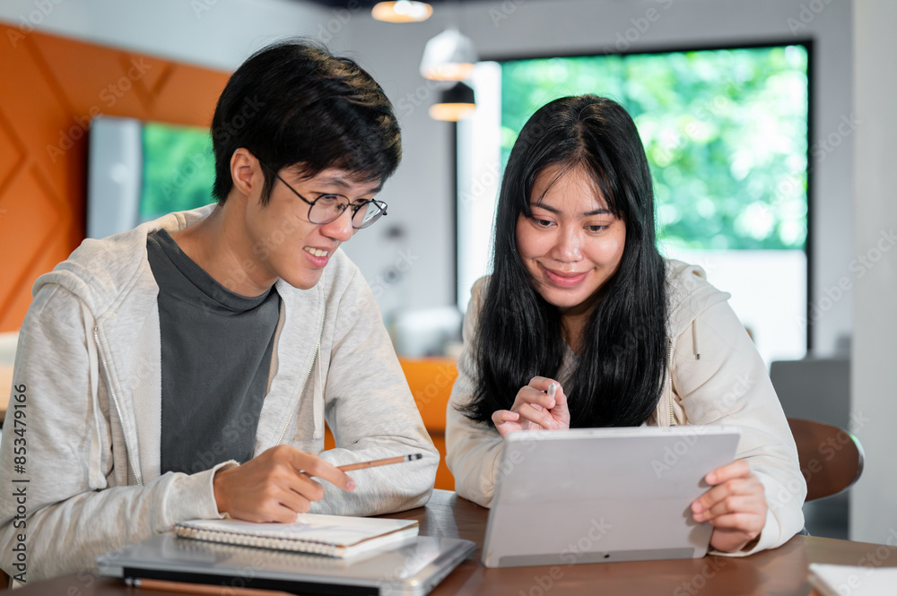 Two Asian college students are studying an online lesson on a tablet together in a coffee shop. Two Asian college students are studying an online lesson on a tablet together in a coffee shop.