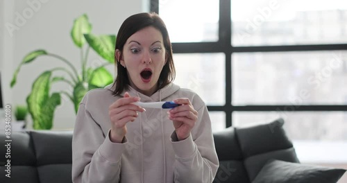 Shocked woman clutches head seeing pregnancy test results photo