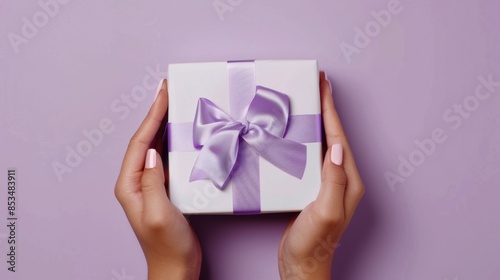 Elegant white gift box with a lavender ribbon held by manicured hands against a pastel background, perfect for special occasions.