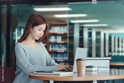 Asian woman student writing notes with textbooks for knowledge, information and literature project in library for research, studying and learning.