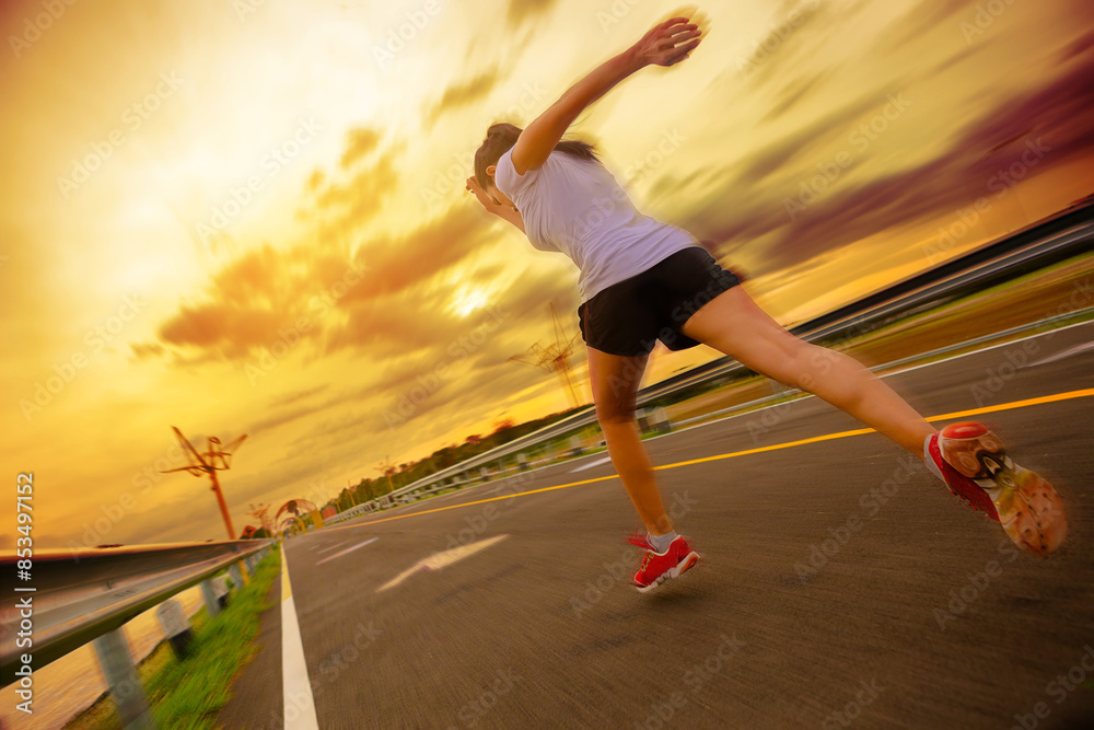 Silhouette of young woman running sprinting on road. Fit runner fitness runner during outdoor workout with sunset background with high speed zoom blur effect. Silhouette of young woman running sprinting on road. Fit runner fitness runner during outdoor workout with sunset background with high speed zoom blur effect.