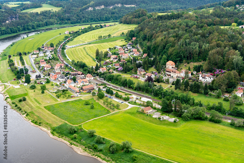 Naklejka premium A small town with a river running through it. The houses are small and spread out. The grass is green and the sky is cloudy