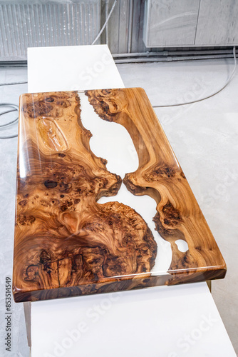 Live edge elm burl slab table top with central epoxy resin river on sawhorses in professional workshop