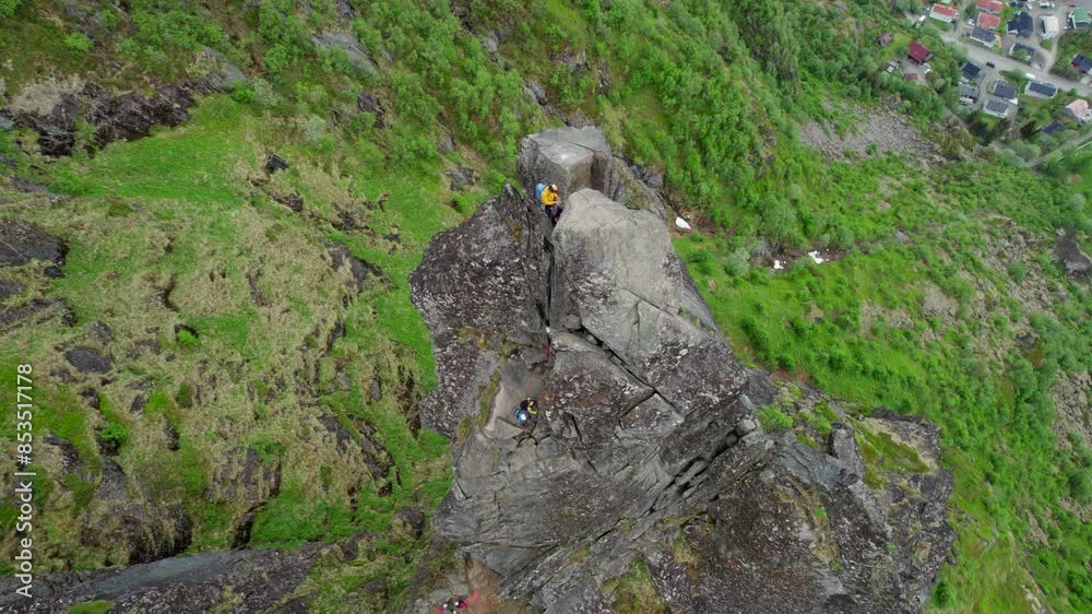 Cinematic aerial view of a climber at the top of the rocky pinnacle of Svolvaergeita (The Goat) in spring. Lofoten, Norway.