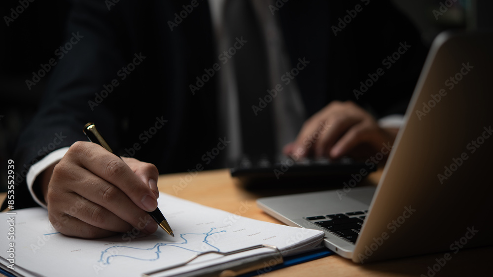 Obraz premium Businessman writing on financial charts, using calculator. Detail-oriented work in finance, accounting. Perfect for business management, financial planning, corporate presentations.