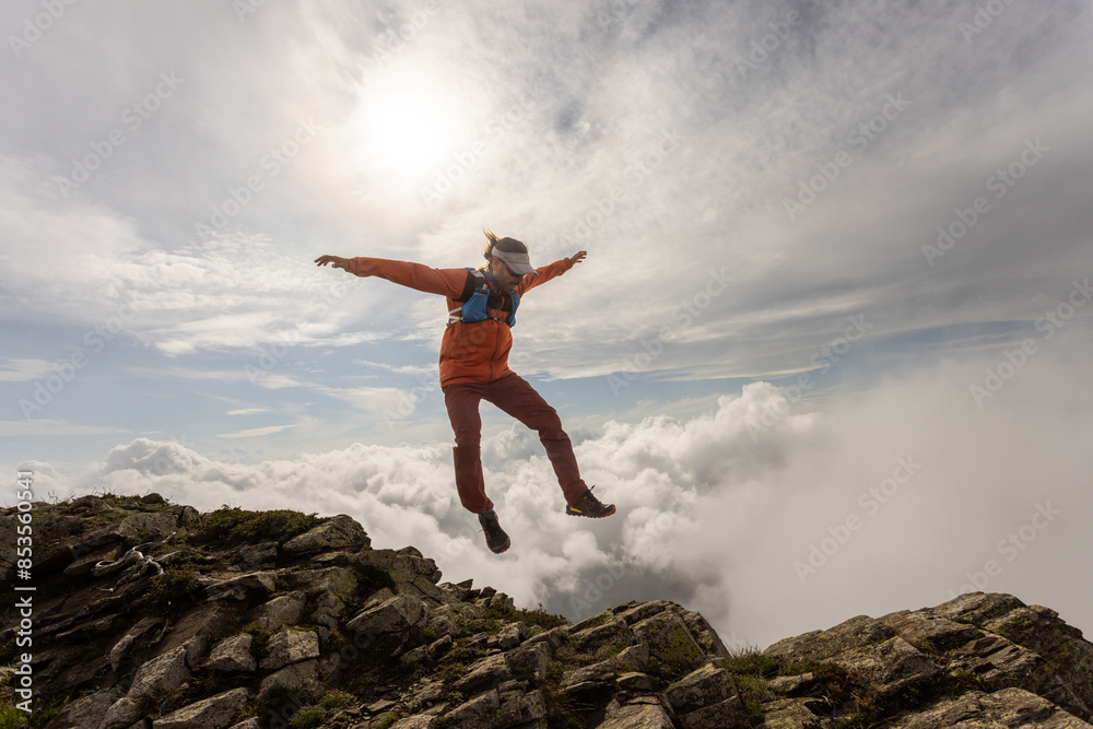 A man is jumping in the air on a mountain. The sky is cloudy and the sun is shining A man is jumping in the air on a mountain. The sky is cloudy and the sun is shining