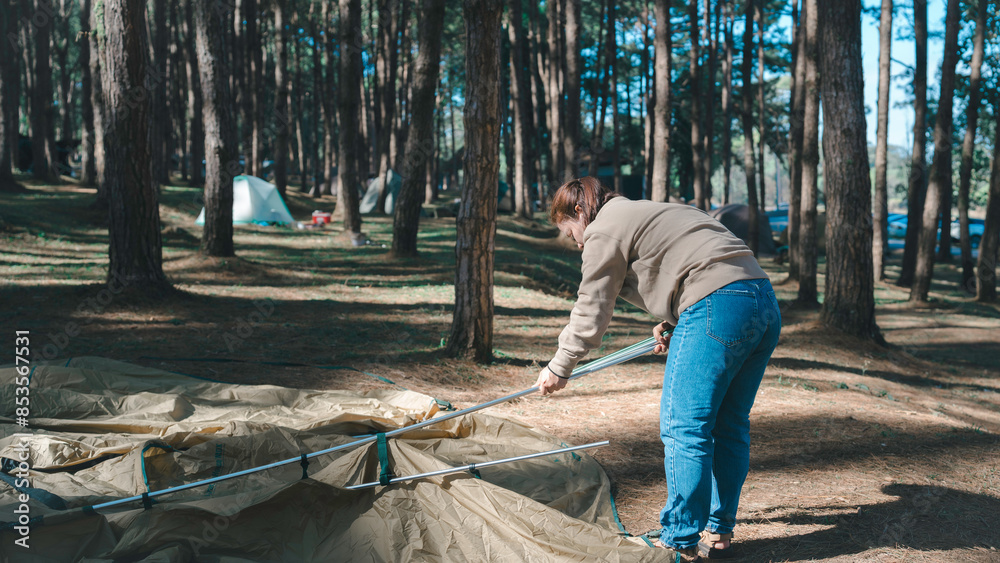 a person setting up a tent in a forest campsite. The scene captures the outdoor activity, nature, and the process of preparing for a camping trip.