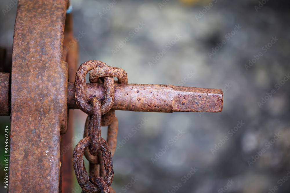 Brown rusty iron chain hanging on rusty holder against a natural background Brown rusty iron chain hanging on rusty holder against a natural background