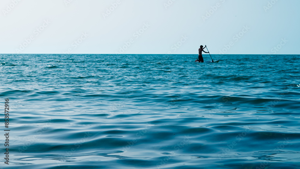 silhouette of person doing sup surfing on the sunset in the blue sea silhouette of person doing sup surfing on the sunset in the blue sea