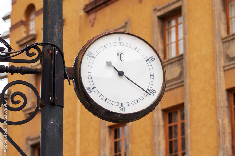 Outdoor Celsius temperature thermometer with clock dial and pointing hand in historic city