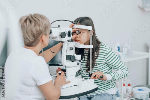 Ophthalmologist using optical instrument for checking girl's eyes
