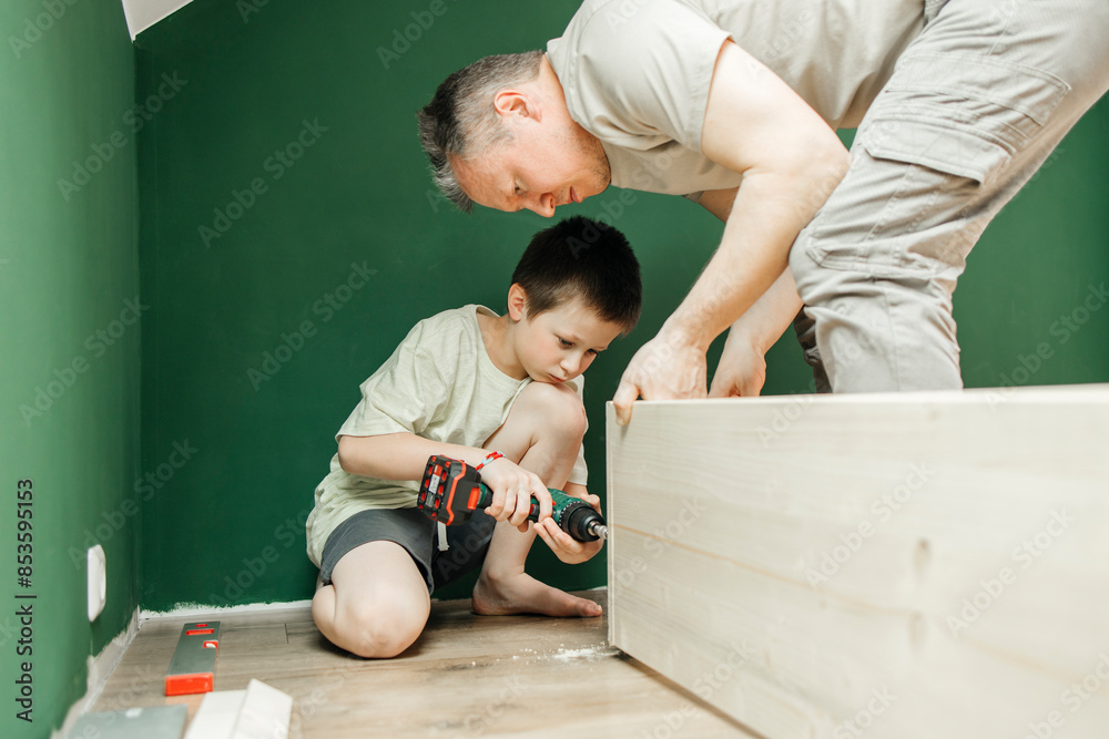 Boy tightening screw on furniture with drill machine near father Boy tightening screw on furniture with drill machine near father
