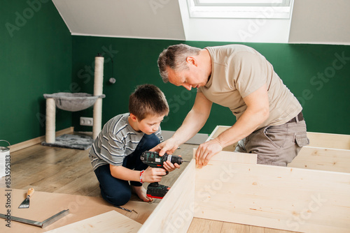 Boy tightening screw on furniture with drill machine near father at home