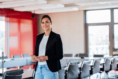 Smiling businesswoman holding smart phone in meeting room at office