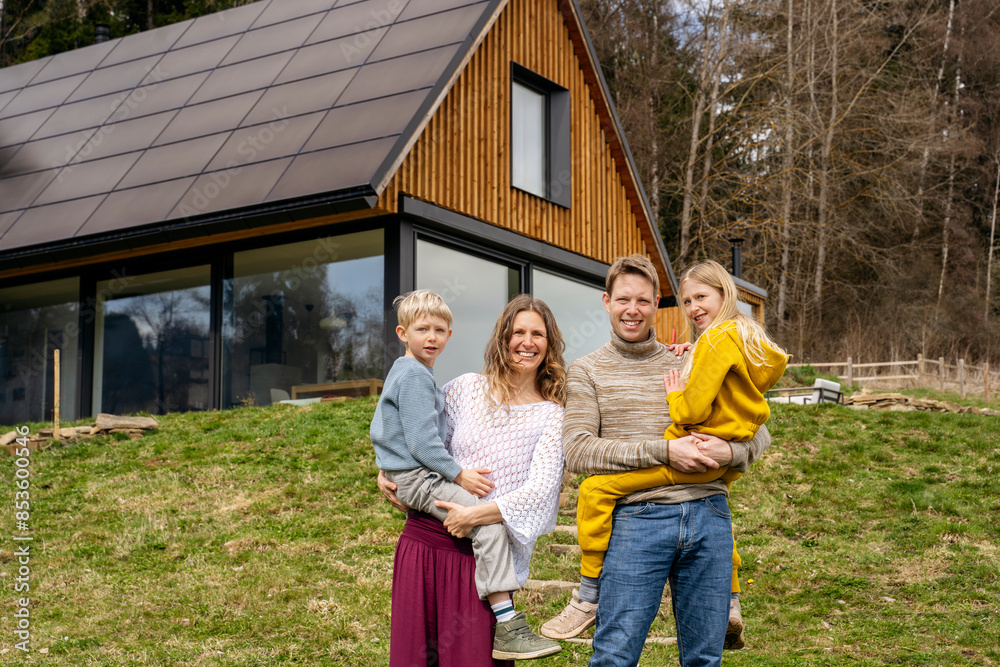 Cheerful mother and father carrying children in front of modern house Cheerful mother and father carrying children in front of modern house