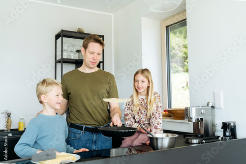 Happy children looking at father flipping pancake in kitchen