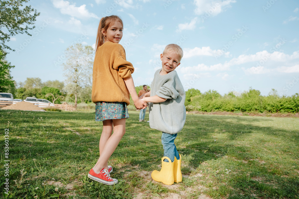 Smiling siblings holding hands and standing at farm Smiling siblings holding hands and standing at farm