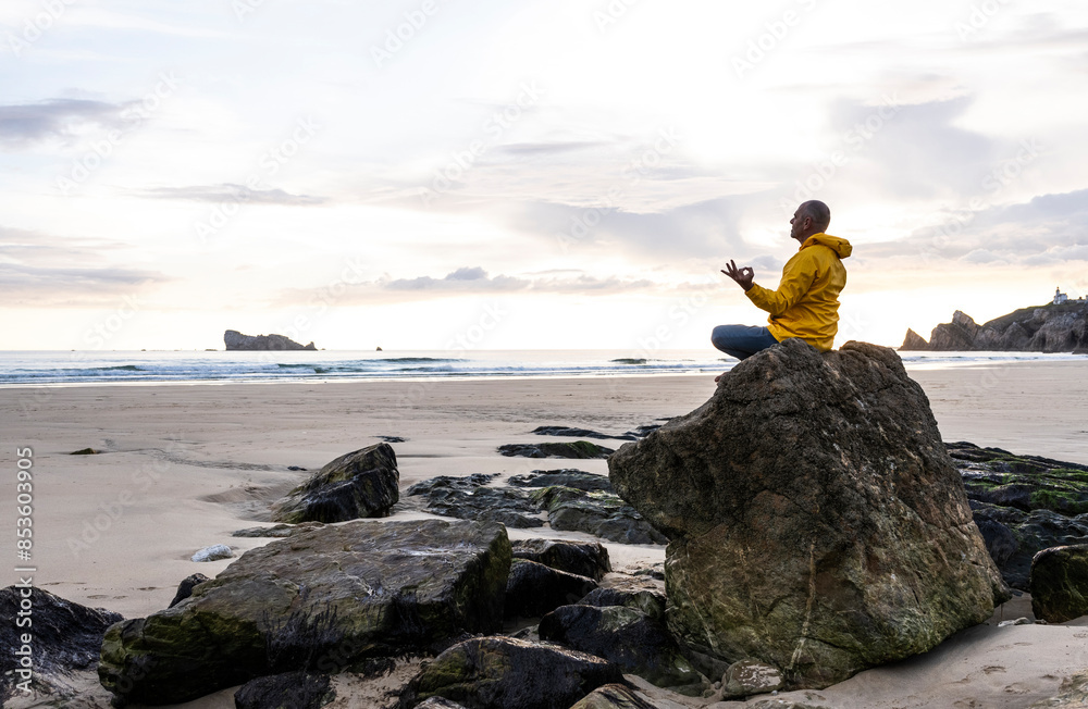 Man practicing yoga on rock at tranquil beach Man practicing yoga on rock at tranquil beach