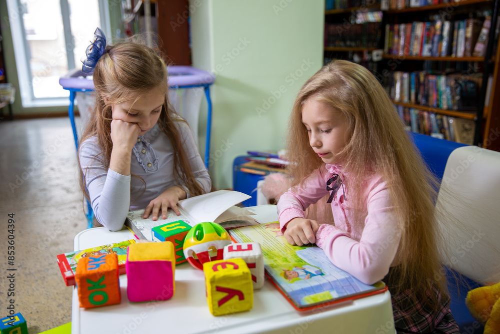 Fototapeta premium Two girls carefully read books in a children library