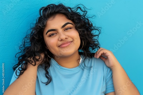 Joyful plus size woman in light blue shirt standing relaxed against blue background