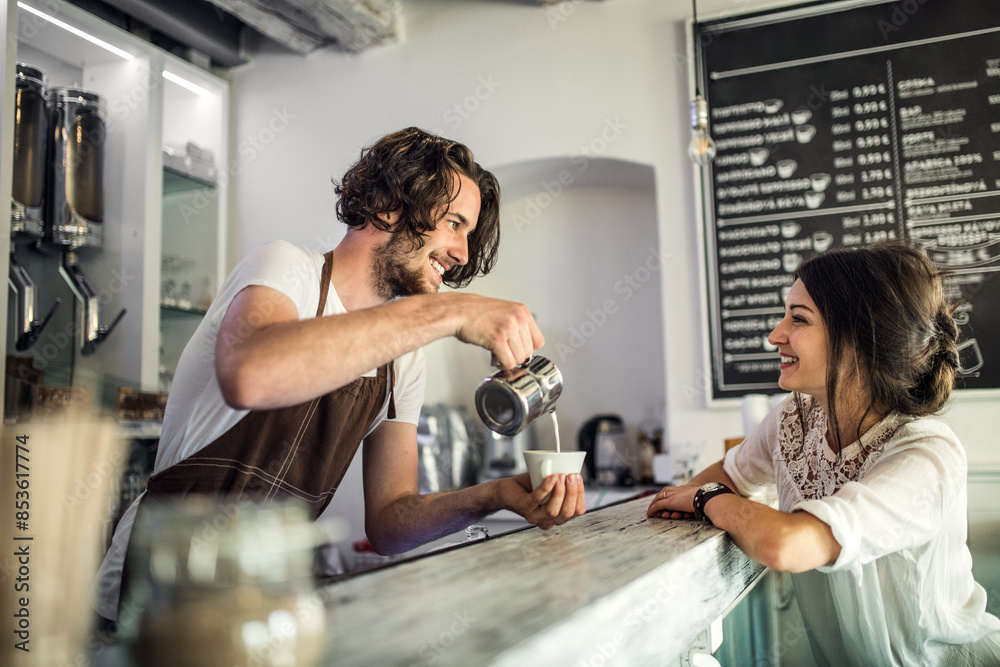 Handsome barista working in coffee shop, preparing coffee for female customer at counter. University student working part-time in cafe. Handsome barista working in coffee shop, preparing coffee for female customer at counter. University student working part-time in cafe.