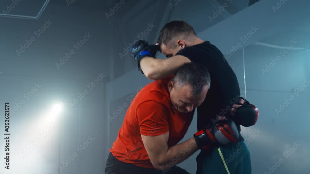 Two fighters show their strength, agility and determination. Athletic fighter in boxing gloves exercises with male trainer. Fighters training at smoky background. 4K, UHD Two fighters show their strength, agility and determination. Athletic fighter in boxing gloves exercises with male trainer. Fighters training at smoky background. 4K, UHD