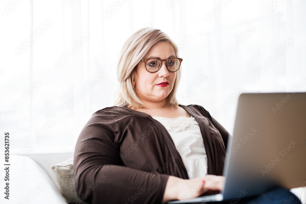 Overweight woman working on laptop from homeoffice, sitting on sofa with legs up. Overweight woman working on laptop from homeoffice, sitting on sofa with legs up.
