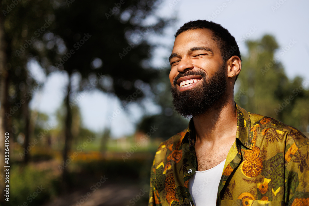 Portrait of happy african american man in shirt standing in sunlight in summer park Portrait of happy african american man in shirt standing in sunlight in summer park