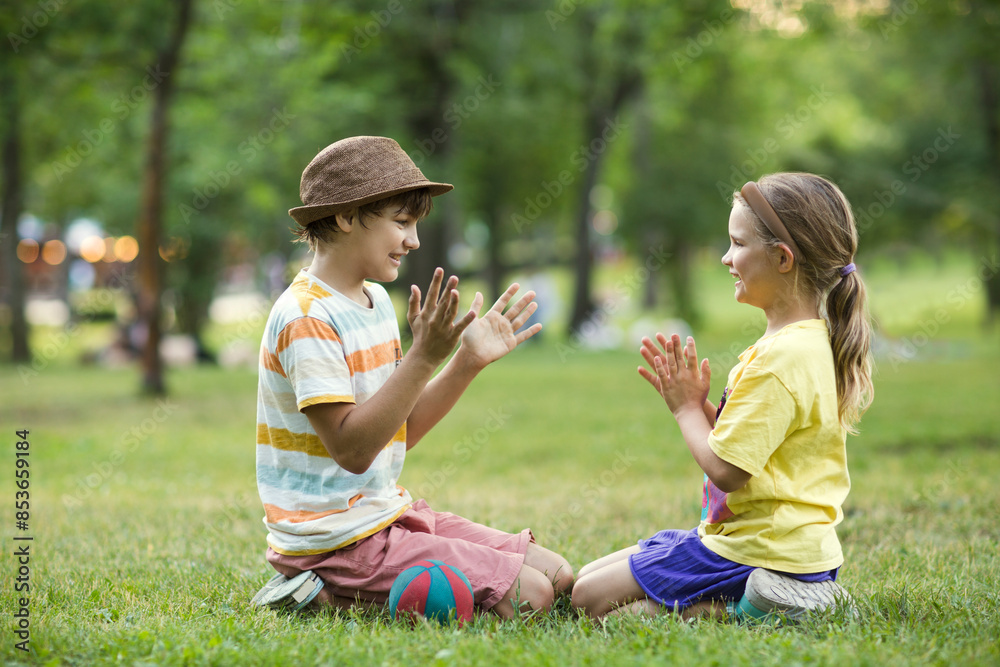 two children brother and sister play sitting on the grass in the park on a summer day. Happy summer holidays two children brother and sister play sitting on the grass in the park on a summer day. Happy summer holidays