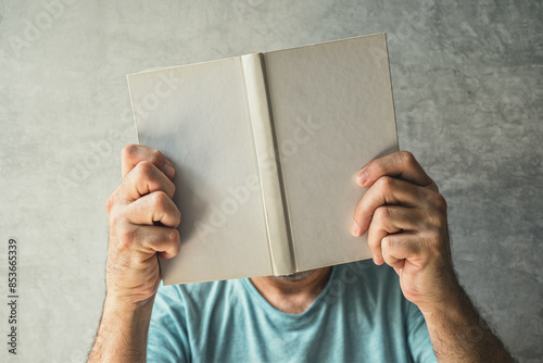 Man reading book, his face is obscured by the hardcover poetry booklet