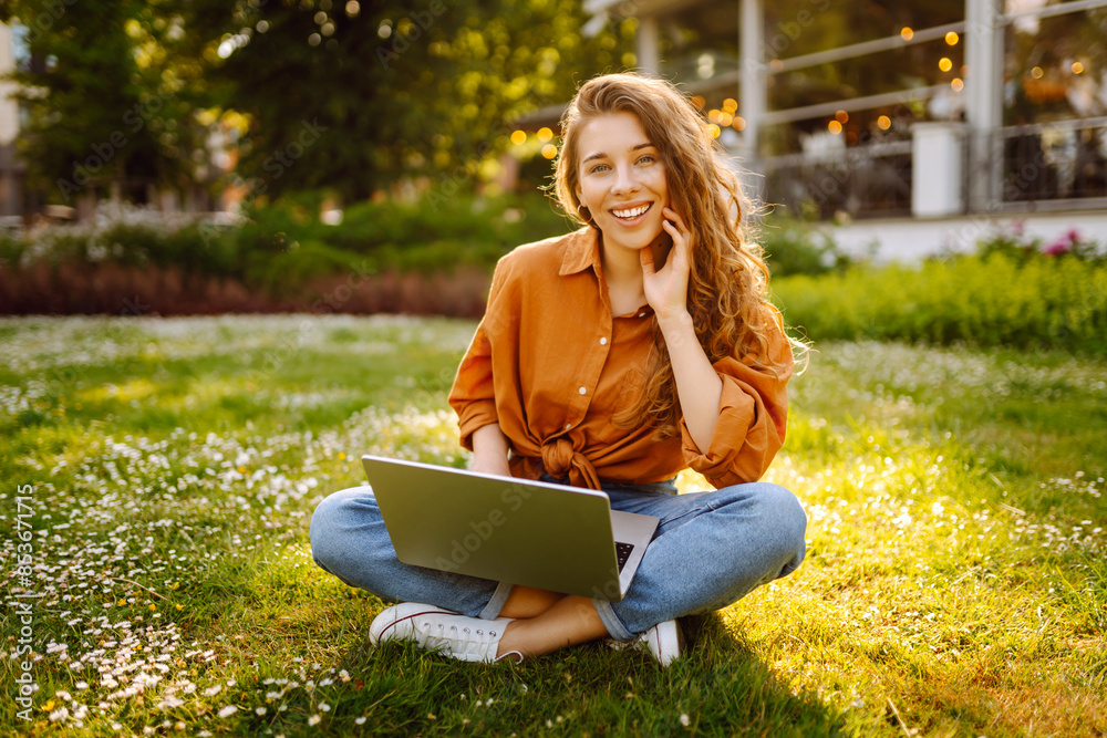 Young woman sits in park communicating by video call. Girl speaking looking at laptop computer, online conference distance office chat, virtual training. Freelance work. Young woman sits in park communicating by video call. Girl speaking looking at laptop computer, online conference distance office chat, virtual training. Freelance work.