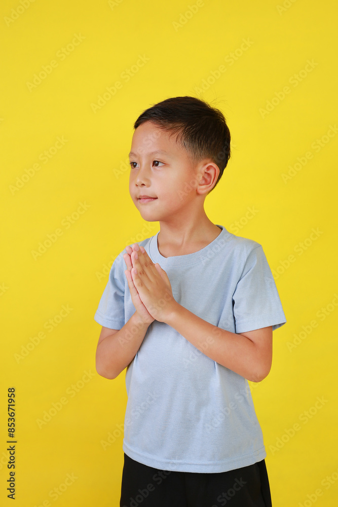 Portrait of Asian boy age about 6 years old Pay respect or pray gesture and looking straight at camera isolated on yellow background. Portrait of Asian boy age about 6 years old Pay respect or pray gesture and looking straight at camera isolated on yellow background.