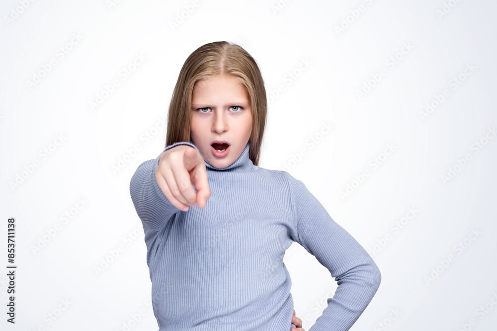 Serious young beautiful teenage girl in a blue knitted turtleneck points her finger at the camera, isolated on a light background. Surprise and advertising concept. Serious young beautiful teenage girl in a blue knitted turtleneck points her finger at the camera, isolated on a light background. Surprise and advertising concept.