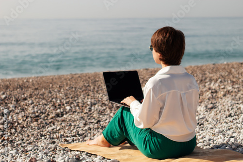 Digital nomad woman traveling the world working with laptop, a girl works on a laptop against the background of the sea on the beach
