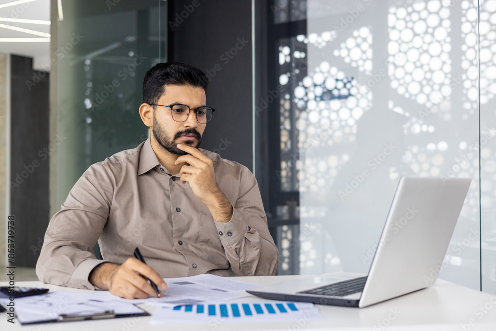 Serious concentrated hispanic businessman financier on paperwork inside office, man in business suit at workplace reviewing and reading papers, contracts and accounts reports. Serious concentrated hispanic businessman financier on paperwork inside office, man in business suit at workplace reviewing and reading papers, contracts and accounts reports.