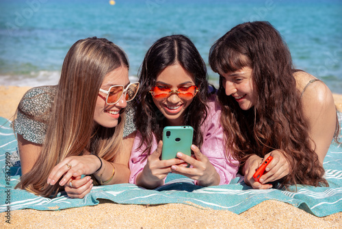 Three young women using apps on their cell phones on the beach © Raquel