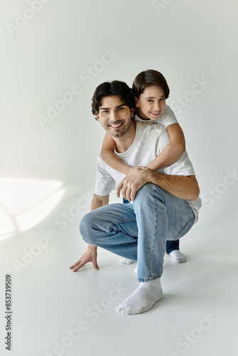 A father and son share a playful moment, the father kneeling and the son hugging him from behind.