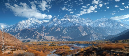 Majestic Snow-Capped Mountain Range with Autumnal Valley Under a Clear Blue Sky