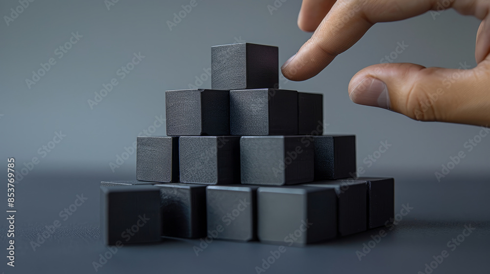 A hand stacking black blocks into a pyramid structure. A hand stacking black blocks into a pyramid structure.