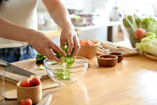 A cropped image of an attractive Asian woman making her healthy salad bowl in the kitchen, putting some lettuces in a bowl. home cooking, healthy and wellness lifestyle, domestic life
