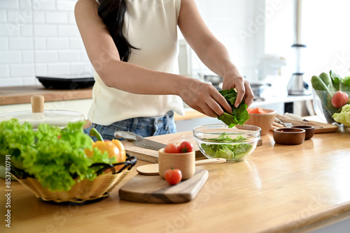 A cropped image of an attractive Asian woman making her healthy salad bowl in the kitchen, putting some lettuces in a bowl. home cooking, healthy and wellness lifestyle, domestic life