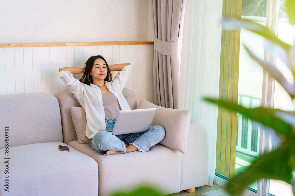 Young Asian woman relaxing and using laptop on a sofa at home in the morning Young Asian woman relaxing and using laptop on a sofa at home in the morning
