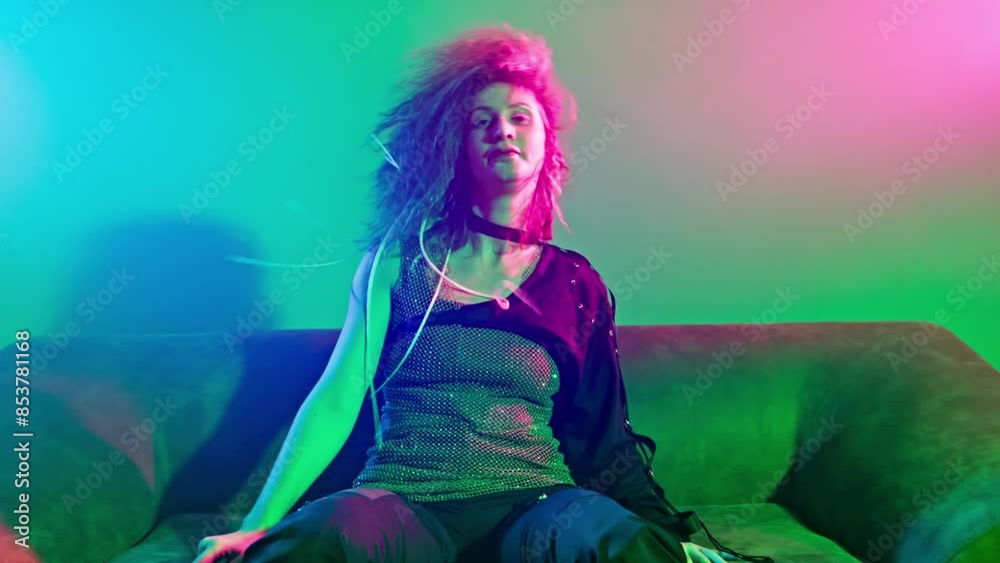 Stylish woman sitting on sofa in smoky room with green, blue and pink lights. Woman dancing experimental dance sitting on couch. Strange emotion. 4K, UHD Stylish woman sitting on sofa in smoky room with green, blue and pink lights. Woman dancing experimental dance sitting on couch. Strange emotion. 4K, UHD