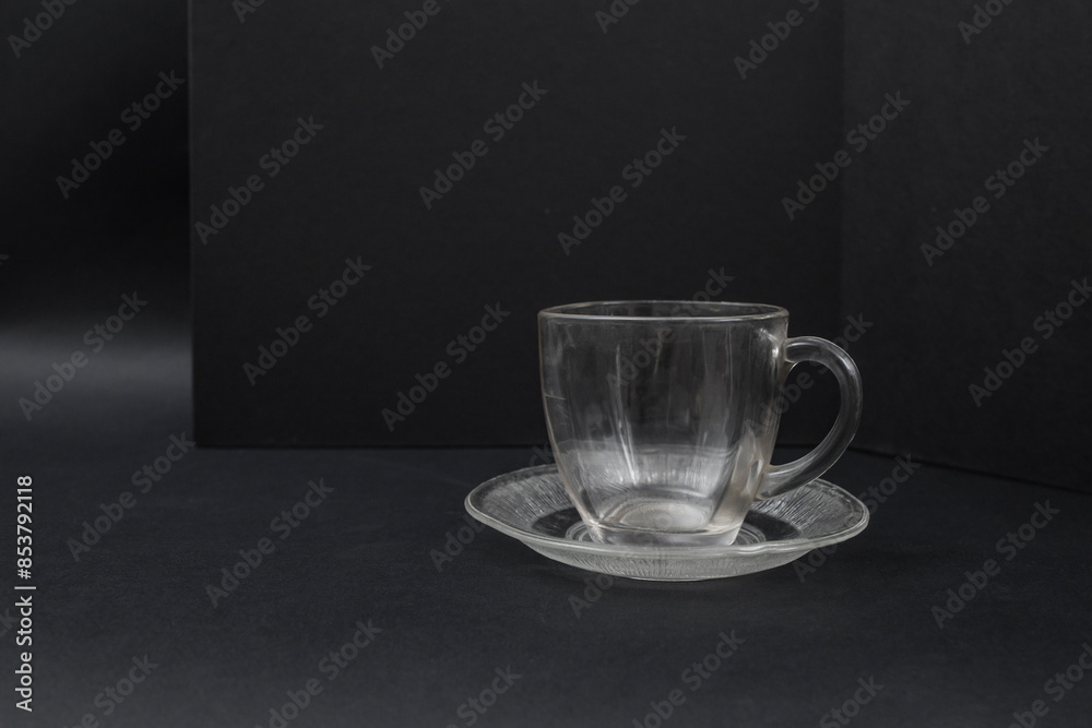 Empty transparent glass cup on a saucer on black background, side view close up Empty transparent glass cup on a saucer on black background, side view close up