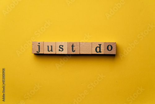 a yellow warm background without shadows wooden cubes with black letters laid out word just do