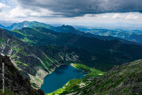 Fototapeta Naklejka Na Ścianę i Meble -  A beautiful shot of a lake from above surrounded by a large mountain range on a cloudy summer day in Poland