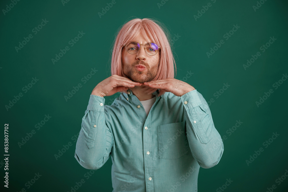 In glasses, posing, having fun. Gay man with pink hair is standing against green background In glasses, posing, having fun. Gay man with pink hair is standing against green background