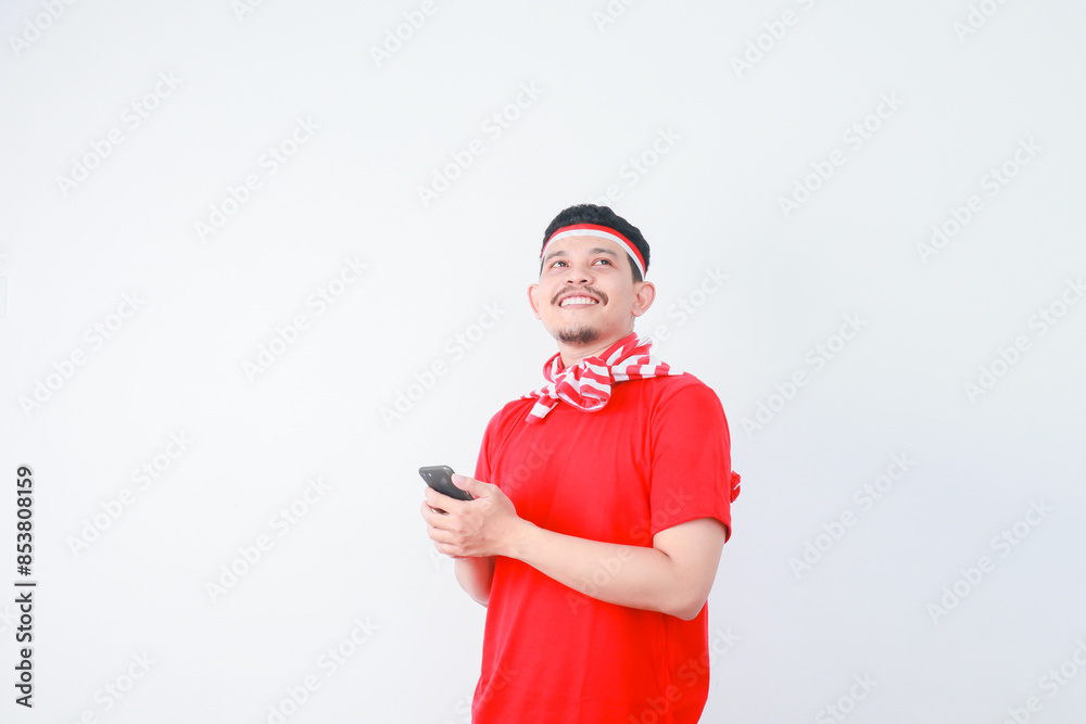 Excited young Asian man in casual t-shirt using mobile phone, getting good news isolated on grey background. indonesian independence day celebration concept Excited young Asian man in casual t-shirt using mobile phone, getting good news isolated on grey background. indonesian independence day celebration concept