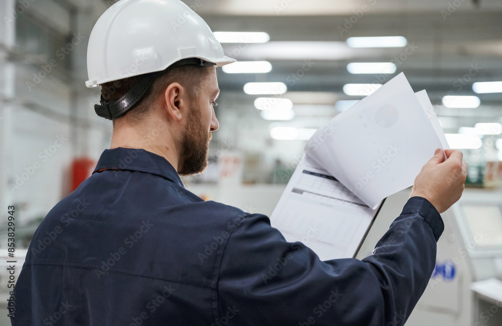 Turning the pages of documents. Factory worker is indoors with hard hat Turning the pages of documents. Factory worker is indoors with hard hat