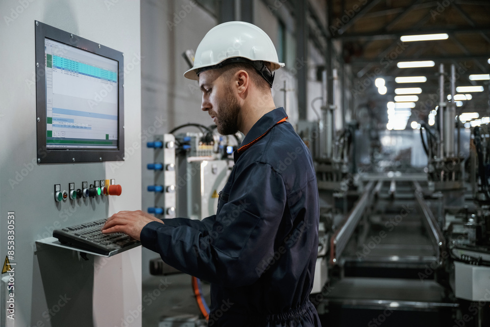 Adjusting settings of machine, operating. Factory worker is indoors with hard hat Adjusting settings of machine, operating. Factory worker is indoors with hard hat